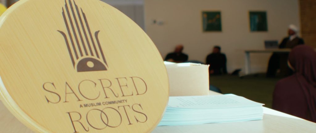 A Sacred Roots coaster on a table, with a gathering in the room behind.